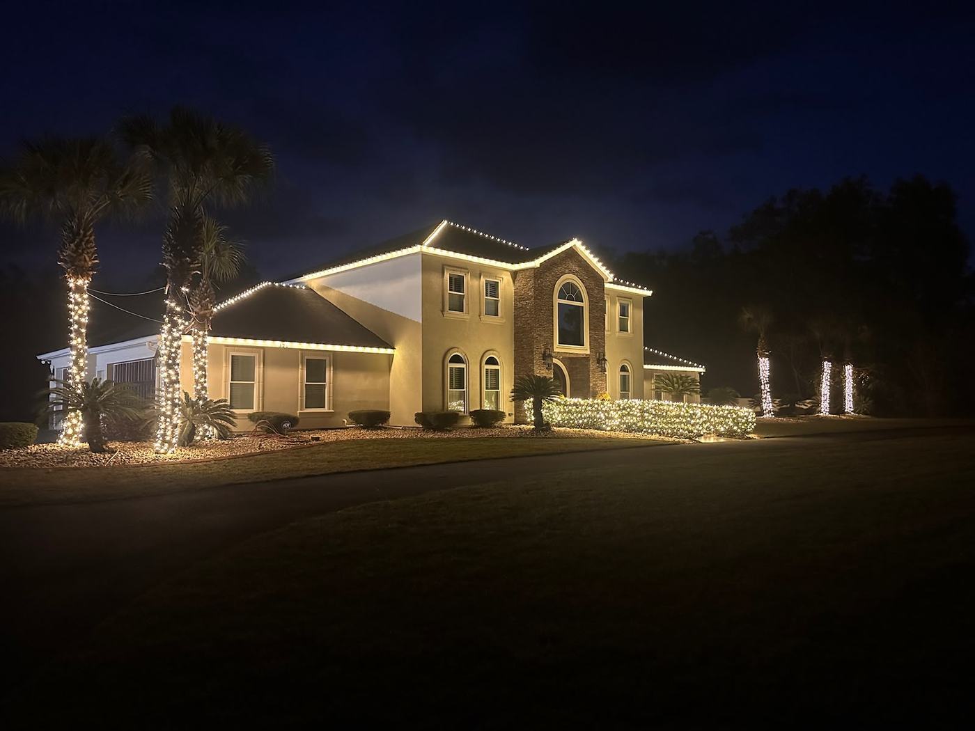 Warm white roofline lighting and wrapped palms on a Tampa stucco home